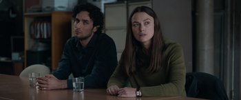 Movie still from “Official Secrets” (2019), directed by Gavin Hood – A woman sitting at a table next to a man in front of a glass of water; Medium shot, Over the shoulder angle