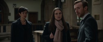 Movie still from “Official Secrets” (2019), directed by Gavin Hood – A woman in a black jacket and a pink scarf; Medium shot, Over the shoulder angle