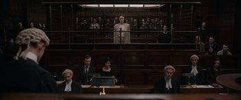 Movie still from “Official Secrets” (2019), directed by Gavin Hood – A man is standing in front of a crowd in a courtroom; Wide shot, High angle