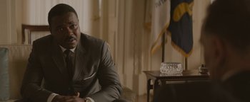 Movie still from “Selma” (2014), directed by Ava DuVernay – A man in a suit sitting in front of an american flag; Close Up shot, Over the shoulder angle
