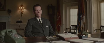Movie still from “Selma” (2014), directed by Ava DuVernay – A man sitting at a desk in a suit and tie in front of a clock; Medium shot, Low angle