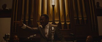 Movie still from “Selma” (2014), directed by Ava DuVernay – A man sitting at a microphone in front of an organ; Medium shot, Low angle