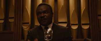 Movie still from “Selma” (2014), directed by Ava DuVernay – A man wearing a suit and tie talking into a microphone; Close Up shot, Over the shoulder angle