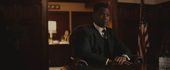 Movie still from “Selma” (2014), directed by Ava DuVernay – A man sitting at a desk wearing a suit and tie; Medium shot, Over the shoulder angle