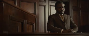 Movie still from “Selma” (2014), directed by Ava DuVernay – A man in a suit sitting in front of a wooden wall; Medium shot, High angle
