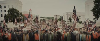 Movie still from “Selma” (2014), directed by Ava DuVernay – A large group of people holding american flags and signs; Extreme Wide shot, High angle