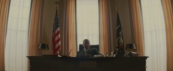 Movie still from “Selma” (2014), directed by Ava DuVernay – A man sitting at a desk in front of two american flags; Medium shot, Low angle