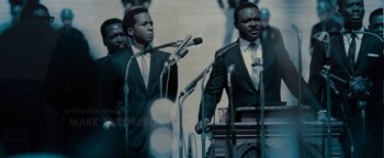 Movie still from “Selma” (2014), directed by Ava DuVernay – A group of men standing next to each other on a stage; Medium shot, Low angle