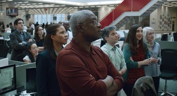 Movie still from “She Said” (2022), directed by Maria Schrader – A group of people standing in a room with their arms crossed; Medium shot, Low angle