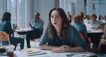 Movie still from “She Said” (2022), directed by Maria Schrader – A woman sitting at a table in front of a group of people; Medium shot, Over the shoulder angle