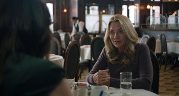 Movie still from “She Said” (2022), directed by Maria Schrader – A woman sitting at a table in front of a glass of water; Medium shot, Over the shoulder angle