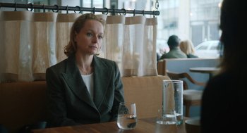 Movie still from “She Said” (2022), directed by Maria Schrader – A woman sitting at a table in front of a glass of water; Medium shot, Over the shoulder angle