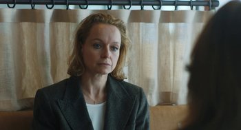 Movie still from “She Said” (2022), directed by Maria Schrader – A woman in a gray jacket is standing in front of a window; Close Up shot, Over the shoulder angle