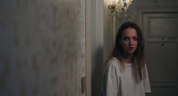 Movie still from “She Said” (2022), directed by Maria Schrader – A woman standing in front of a wall with a chandelier; Medium shot, Over the shoulder angle