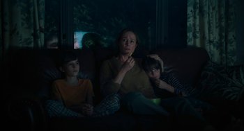 Movie still from “She Said” (2022), directed by Maria Schrader – A woman and two children sitting on a couch; Medium shot, Low angle