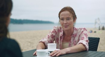 Movie still from “She Said” (2022), directed by Maria Schrader – A woman sitting at a table on the beach with two cups; Close Up shot, Over the shoulder angle