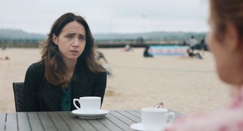 Movie still from “She Said” (2022), directed by Maria Schrader – A woman sitting at a table with two cups of coffee; Medium shot, Over the shoulder angle