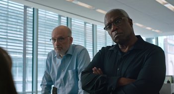 Movie still from “She Said” (2022), directed by Maria Schrader – Two men are standing next to each other in a room; Medium shot, Low angle