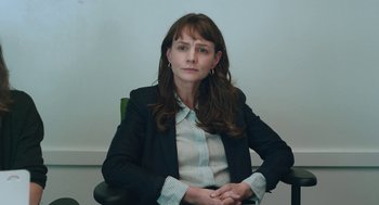 Movie still from “She Said” (2022), directed by Maria Schrader – A woman sitting in an office chair wearing a suit; Close Up shot, High angle
