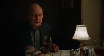 Movie still from “She Said” (2022), directed by Maria Schrader – An older man sitting at a table with a glass of wine; Close Up shot, Over the shoulder angle