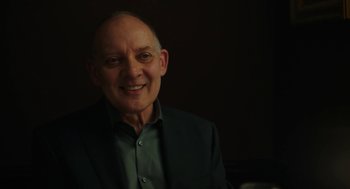 Movie still from “She Said” (2022), directed by Maria Schrader – An older man wearing a suit and smiling for the camera; Close Up shot, Over the shoulder angle