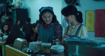 Movie still from “She Said” (2022), directed by Maria Schrader – Two young women are smiling at each other in a kitchen; Medium shot, Over the shoulder angle