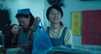 Movie still from “She Said” (2022), directed by Maria Schrader – A woman holding a blue bag in a room with other women; Medium shot, Low angle