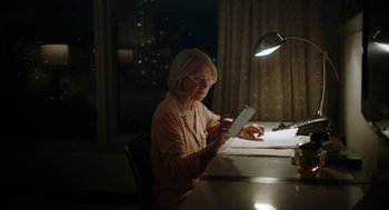 Movie still from “She Said” (2022), directed by Maria Schrader – An older woman sitting at a table looking at a tablet; Medium shot, High angle