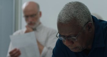 Movie still from “She Said” (2022), directed by Maria Schrader – A man sitting next to another man in a white shirt; Close Up shot, Over the shoulder angle