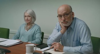 Movie still from “She Said” (2022), directed by Maria Schrader – An older man and woman sitting in front of a table; Medium shot, Over the shoulder angle