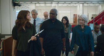 Movie still from “She Said” (2022), directed by Maria Schrader – A group of people standing around each other in a room; Medium shot, Low angle