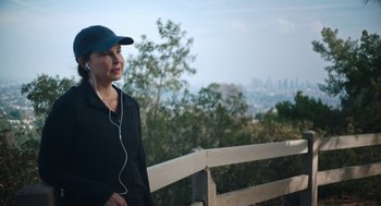 Movie still from “She Said” (2022), directed by Maria Schrader – A person wearing a hat and ear buds standing next to a railing; Close Up shot, High angle