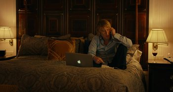 Movie still from “She's Funny That Way” (2014), directed by Peter Bogdanovich – A person sitting on a bed with a laptop; Medium shot, High angle