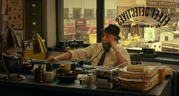 Movie still from “She's Funny That Way” (2014), directed by Peter Bogdanovich – An older man sitting at a counter talking on a phone; Medium shot, Over the shoulder angle