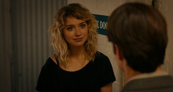 Movie still from “She's Funny That Way” (2014), directed by Peter Bogdanovich – A young woman looking into a mirror while standing in front of a wall; Close Up shot, Over the shoulder angle