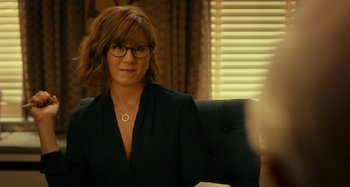 Movie still from “She's Funny That Way” (2014), directed by Peter Bogdanovich – A woman sitting in a chair wearing glasses; Close Up shot, Over the shoulder angle
