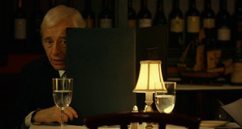 Movie still from “She's Funny That Way” (2014), directed by Peter Bogdanovich – A man sitting in front of a computer at a table; Medium shot, Over the shoulder angle
