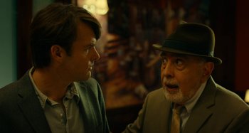 Movie still from “She's Funny That Way” (2014), directed by Peter Bogdanovich – A man in a suit and a hat talking to another man in a suit; Close Up shot, Over the shoulder angle