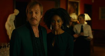 Movie still from “She's Funny That Way” (2014), directed by Peter Bogdanovich – A man standing next to a woman in front of a crowd; Close Up shot, Over the shoulder angle