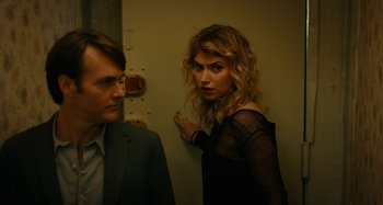 Movie still from “She's Funny That Way” (2014), directed by Peter Bogdanovich – A man and a woman standing next to each other in a room; Close Up shot, Over the shoulder angle