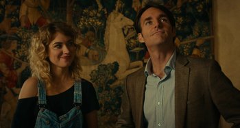 Movie still from “She's Funny That Way” (2014), directed by Peter Bogdanovich – A man and a woman standing next to each other in front of a mural; Medium shot, Low angle