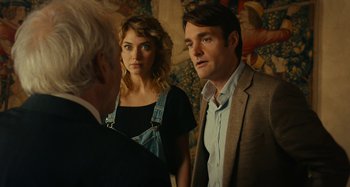 Movie still from “She's Funny That Way” (2014), directed by Peter Bogdanovich – A man and a woman standing next to each other in front of an older man; Medium shot, Over the shoulder angle