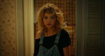 Movie still from “She's Funny That Way” (2014), directed by Peter Bogdanovich – A woman with curly hair wearing a black shirt and blue overalls; Close Up shot, Over the shoulder angle