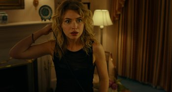 Movie still from “She's Funny That Way” (2014), directed by Peter Bogdanovich – A woman in a black top is standing in a room; Close Up shot, Over the shoulder angle