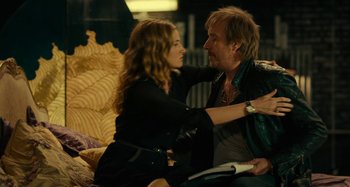 Movie still from “She's Funny That Way” (2014), directed by Peter Bogdanovich – A man and a woman sitting on a couch arm in arm; Medium shot, Over the shoulder angle