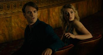 Movie still from “She's Funny That Way” (2014), directed by Peter Bogdanovich – A man and a woman sitting next to each other; Medium shot, Low angle