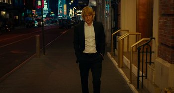 Movie still from “She's Funny That Way” (2014), directed by Peter Bogdanovich – A man standing on a sidewalk in front of a building; Medium shot, Low angle
