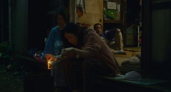 Movie still from “Shoplifters” (2018), directed by Kore-eda Hirokazu – A group of people sitting around a fire; Medium shot, High angle