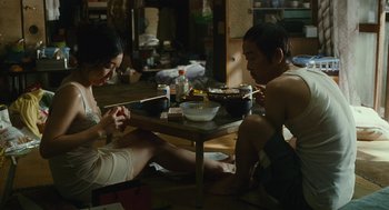 Movie still from “Shoplifters” (2018), directed by Kore-eda Hirokazu – A man and a woman sitting at a table eating food; Medium shot, High angle