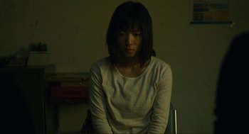 Movie still from “Shoplifters” (2018), directed by Kore-eda Hirokazu – A woman sitting in a chair in a dark room; Medium shot, High angle